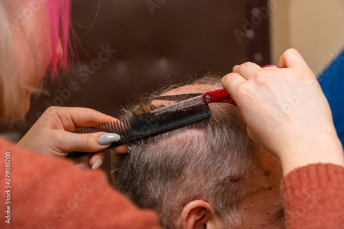Woman hairdresser cuts a man with a receding hairline with scissors. Selective focus