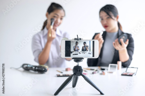 Business online on social media, Two Beautiful Woman Blogger is showing present tutorial beauty cosmetic product and broadcast live streaming video to social network while recording teaching online © Ngampol
