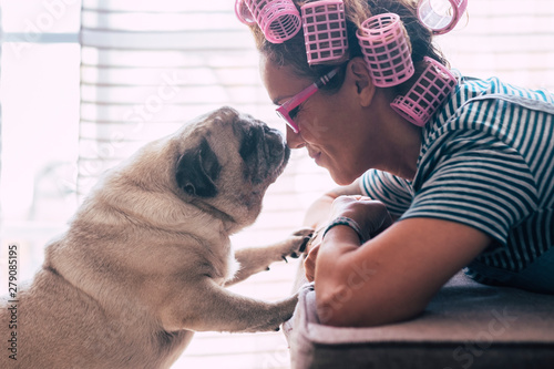 Love and friendship concept with pretty caucasian young woman lay down on the sofa at home and lovely adorable pug dog kissing her on the nose - curlers on head for getting ready activity photo