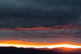 View of dark clouds at sunset, with sun filtering through an hole over the mountains