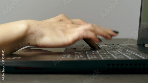 Young woman writes fast on notebook keyboard. Side view. Beautiful manicure on nails.
