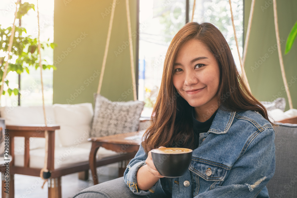 Closeup image of a beautiful asian woman holding and drinking hot coffee in cafe Closeup image of a beautiful asian woman holding and drinking hot coffee in cafe