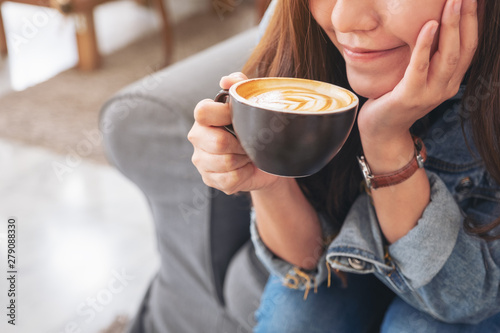 Closeup image of a beautiful asian woman holding and drinking hot coffee in cafe
