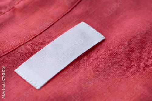 White blank clothing tag label on red linen shirt fabric texture background