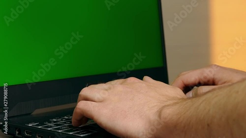 Man waiting with hands on notebook keyboard with all fingers with greenscreen. View from the side.