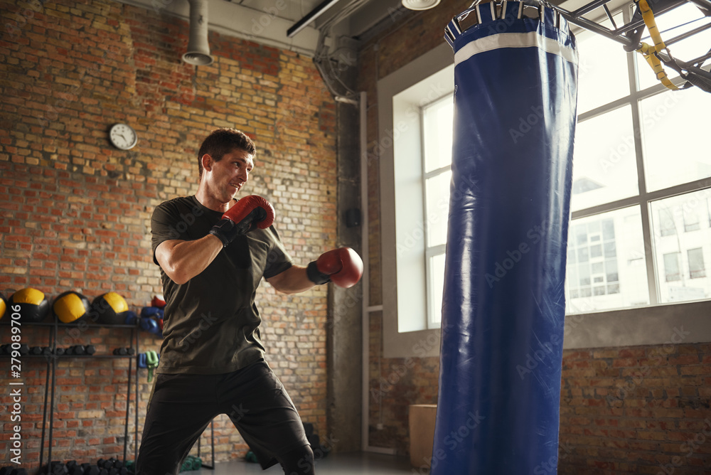 Strong and motivated. Young and sporty man boxing in gloves in a loft style gym. Boxer