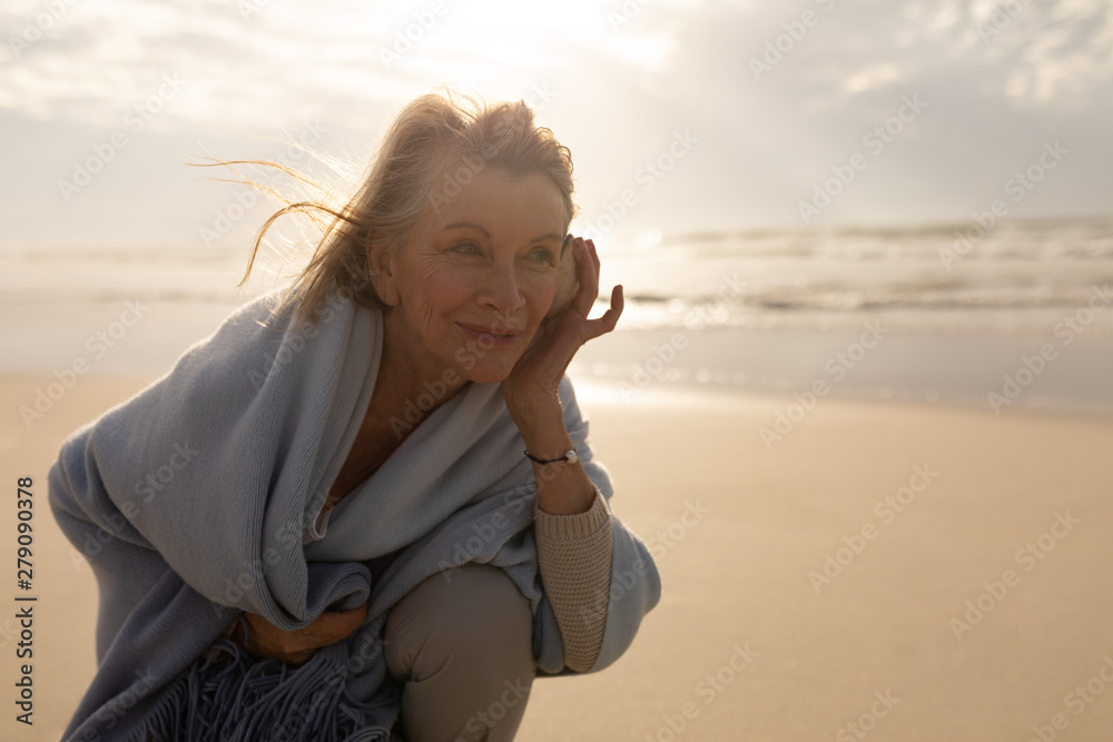 Senior woman wrapped in a shawl holding sea shell at beach