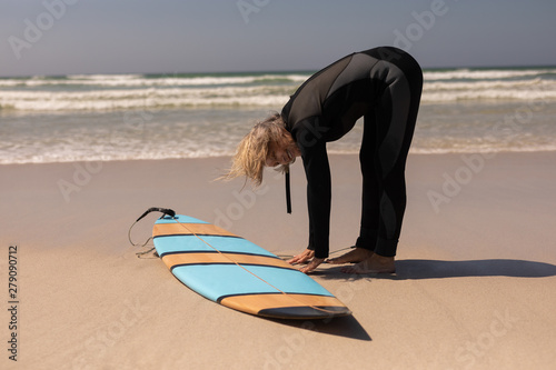 Side view of senior female surfer with surfboard exercising on the beach