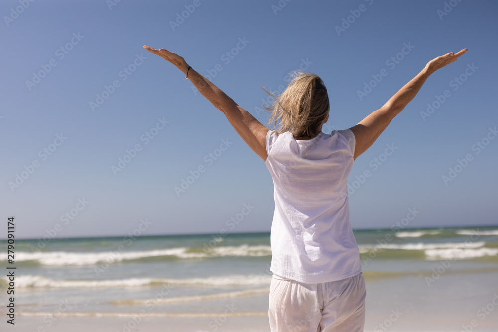 Rear view of senior woman standing with arms outstretched at beach 