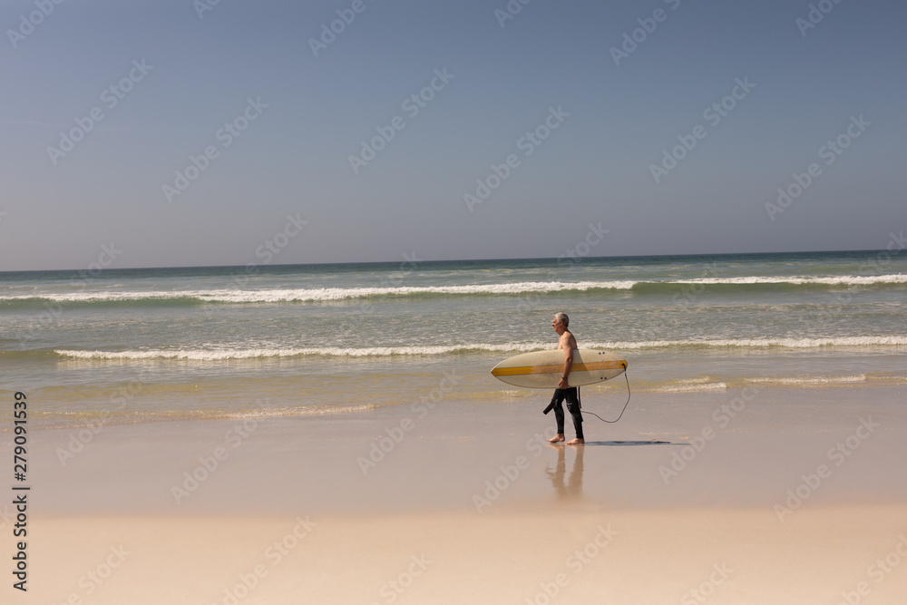 Side view of senior male surfer walking with surfboard on the beach