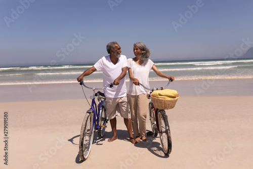 Senior couple walking with bicycle and looking each other on beach