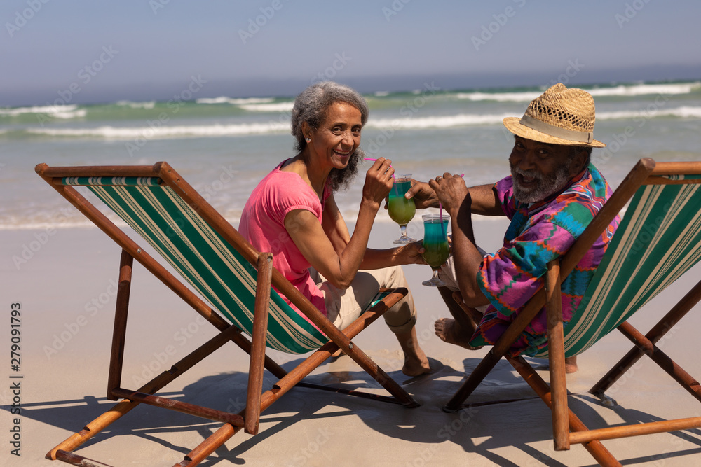 Senior couple relaxing on sun lounger and drinking cocktail on beach