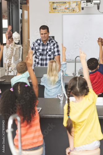 School kids raising hand while teacher asking question 