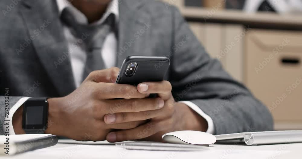 Young african man in a modern office, using a smartphone at the workplace, close-up of hands, office interior on a background. Young african man in a modern office, using a smartphone at the workplace, close-up of hands, office interior on a background.