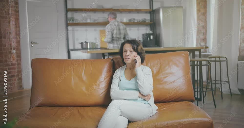 Senior woman talks on phone while her husband wipes plates Senior woman talks on phone while her husband wipes plates