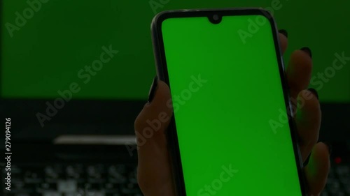 Young woman looks on her smartphone with greenscreen with notebook in the background with greenscreen.