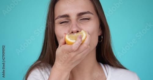 Young girl eats a lemon. Portrait of a beautiful woman. Girl grimaces while eating a sour lemon. Slow motion. Turquoise background.