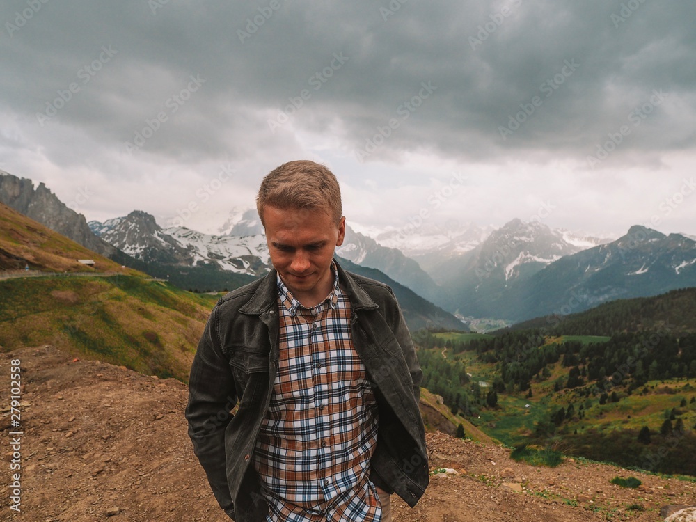 A young man in a plaid shirt stands against the background of the Dolomites. Mountain summer landscape in the Dolomites in Northern Italy.