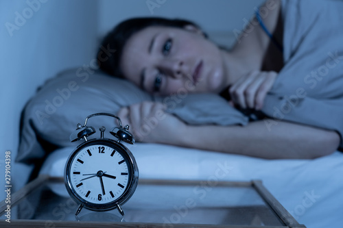 Attractive woman in bed staring at alarm clock trying to sleep feeling stressed and sleepless photo