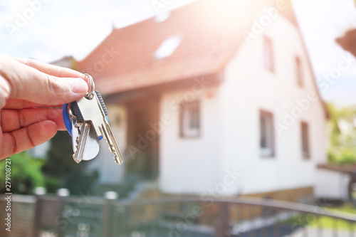 Keys in hand against the background of a blurred house with a sun flare.