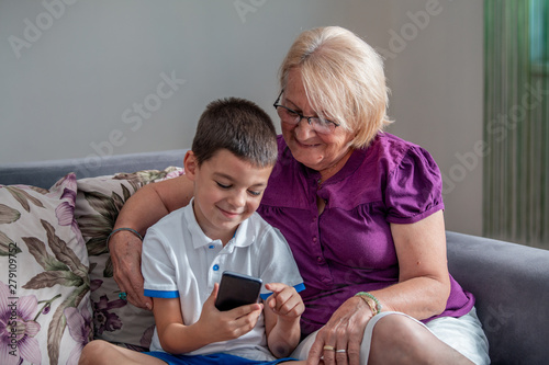 Attentive grandma pointing finger in mobile. Smiling boy keeping it in hand. Communication and technology concept © Graphicroyalty