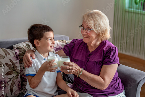 Happy little grandson drinks milk with straw in glass with grandmother. Use of calcium. Beautiful grandma with grandson drinking milk, healthcare concept.
