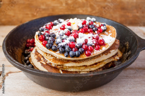 Homemade pancakes on a black cast iron skillet with berries on wooden background vintage tableware