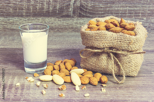 Ripe unpeeled almonds in a hemp sack and almond milk in a glass on a wooden backround. Food photography. Minimalist photography.