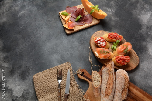 Brushetta or traditional Spanish tapas. Appetizers with Italian antipasti snacks. Variety of small sandwiches with cherry tomatoes, salmon, cream cheese. Prosciutto served with melon and basil