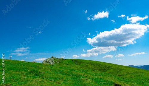 Landscape of green grass and rock hill in spring with beautiful blue sky and white clouds. Countryside or rural view. Nature background in sunny day. Fresh air environment. Stone on the mountain.