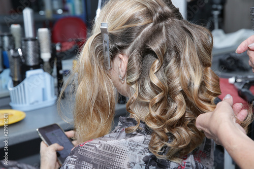 Close-up. Young blonde woman with long hair in hair salon. Barber makes a hairdress to blonde  curling curls. Concept for hairdressers and barbershop.