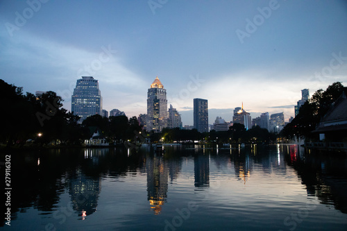 View of Lumphini Park lake with buildings in Bangkok with sunset light