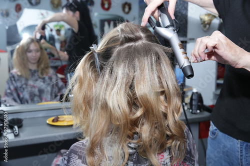 Close-up. Young blonde woman with long hair in hair salon. Barber makes a hairdress to blonde, curling curls. Concept for hairdressers and barbershop.