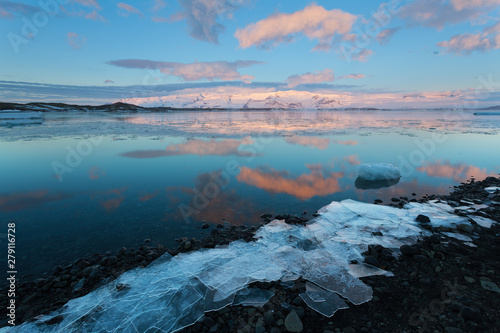 Icebergs float on Jokulsarlon glacier lagoon at sunrise, with background mountain peaks lit by sunrise, in Iceland.