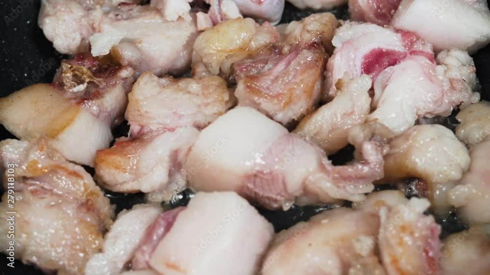 Closeup of pork bits being fried in a dish lined with coconut oil and being gently stirred by a cook Closeup of pork bits being fried in a dish lined with coconut oil and being gently stirred by a cook