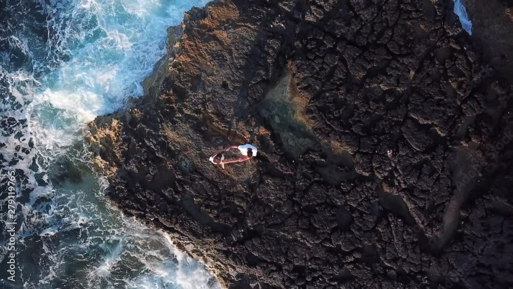 Top down drone shot in slow motion of an in love couple dancing on a cliff, the stormy waves are crushing against the coast in malta. Top down drone shot in slow motion of an in love couple dancing on a cliff, the stormy waves are crushing against the coast in malta.