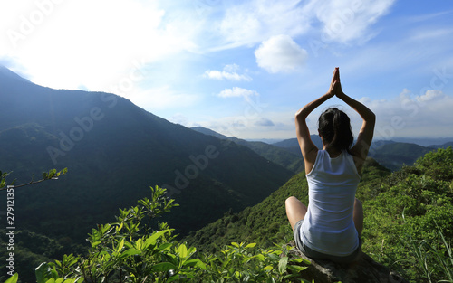 Yoga woman meditating on mountain peak cliff edge in the sunrise