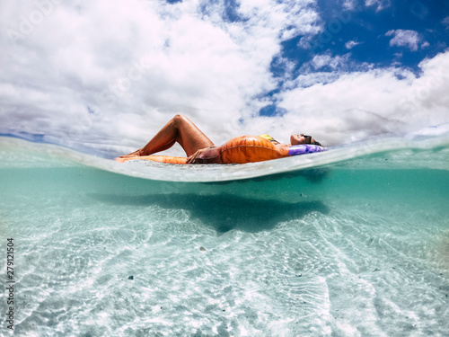 Fototapeta Naklejka Na Ścianę i Meble -  Beautiful tanned young woman lay down and relax on a trendy inflatable lilo in a paradise beach with sand and clear blue water - underwater and out image for vacation and travel concept lifestyle