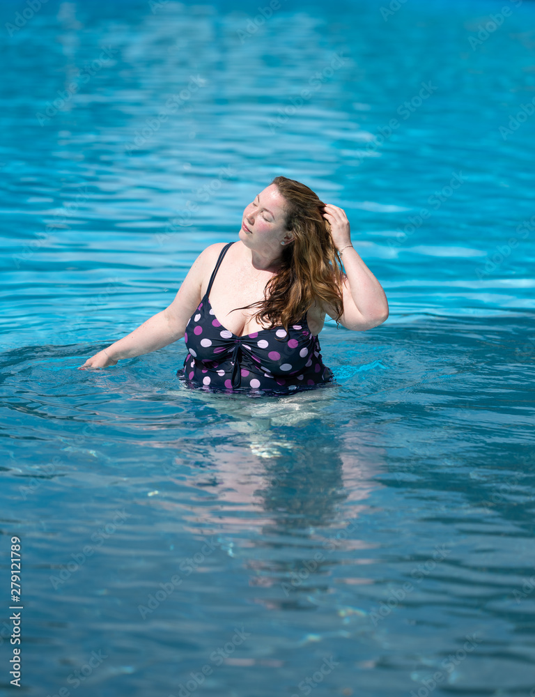 confident large plus size model in swimming pool wearing tankini touching long hair on a sunny summer day