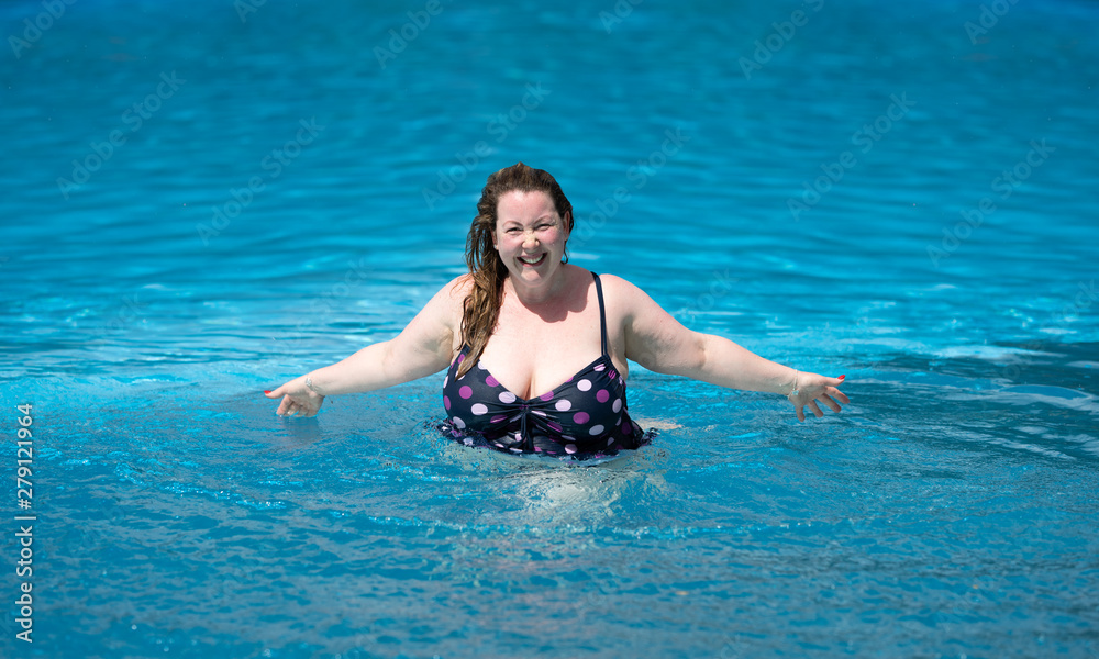 confident large plus size woman having fun in a swimming pool on a sunny summer day looking at camera smiling