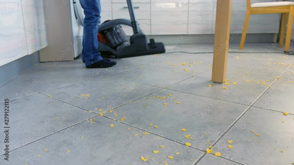 Little boy vacuuming the kitchen floor. He tidies up the corn flakes ...