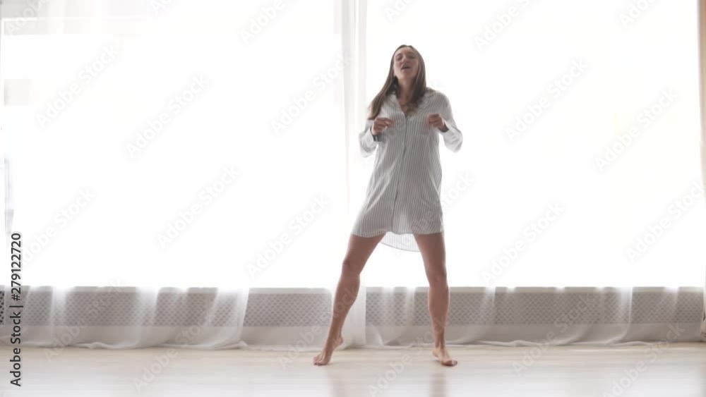 Cheerful young woman dancing in the morning in a nightgown by the window