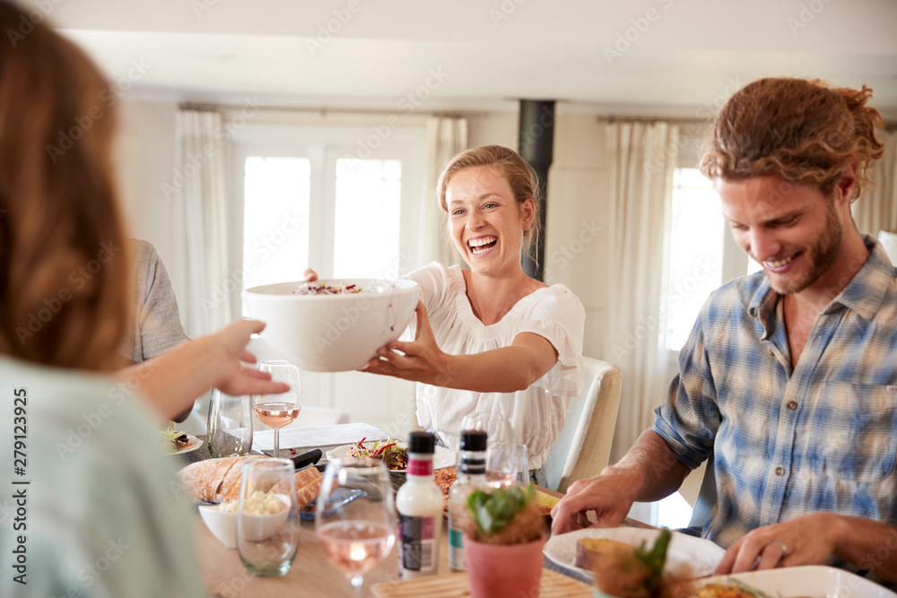 Young adult friends passing food across during lunch at a dinner table, close up Young adult friends passing food across during lunch at a dinner table, close up