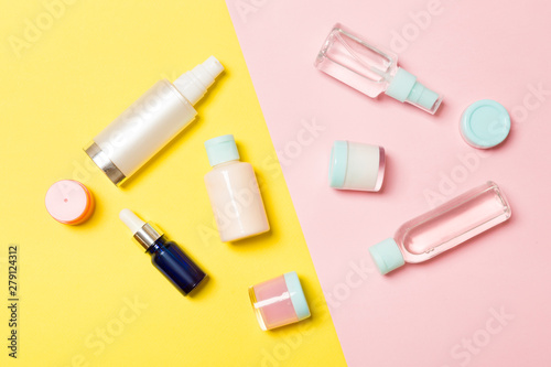 Top view of different cosmetic bottles and container for cosmetics on pink and yellow background. Flat lay composition with copy space