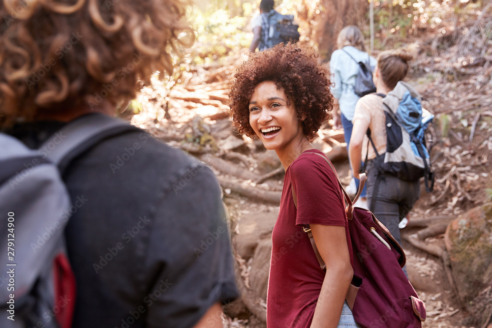 Group of millennial  friends hiking uphill on a forest trail, waist up