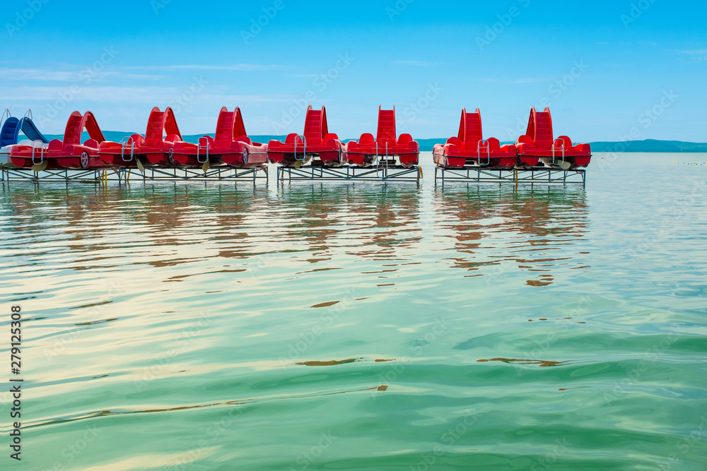 Travel background of red pedal boats on a pier with big water surface in the front at lake Balaton in Hungary
