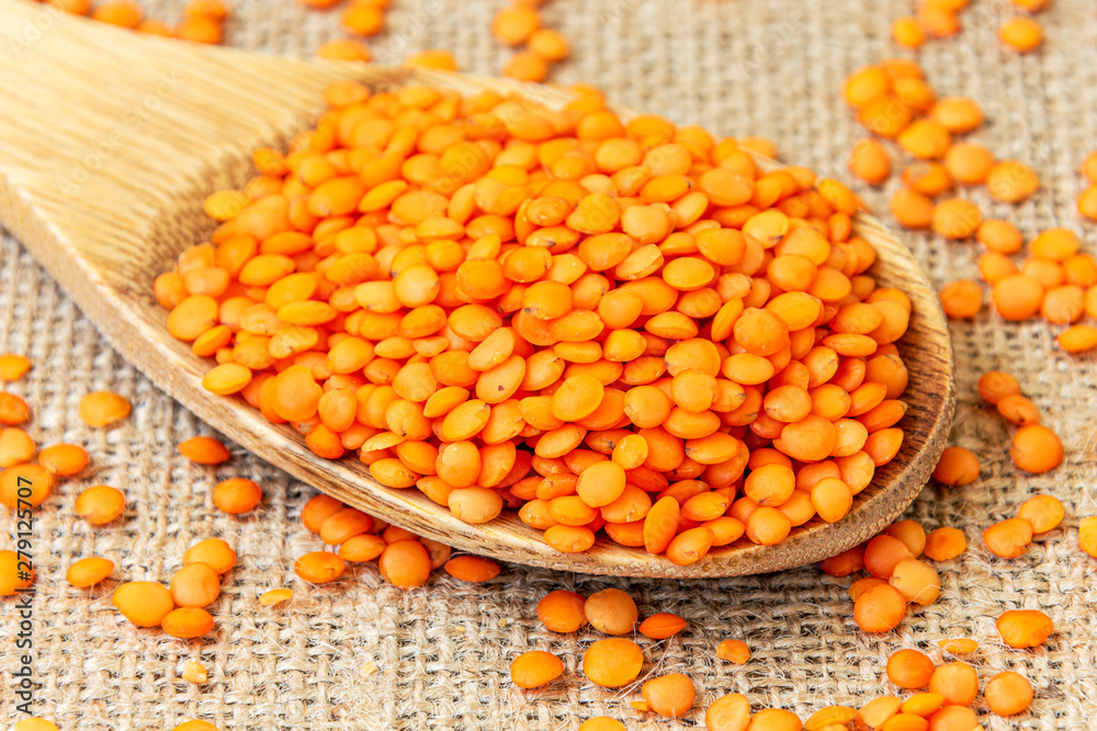 Red lentils in a wooden spoon on a background of burlap. Product photo of red lentils. Healthy lifestyle. Vegetarian and vegan diet. Spilled lens Red lentils in a wooden spoon on a background of burlap. Product photo of red lentils. Healthy lifestyle. Vegetarian and vegan diet. Spilled lens