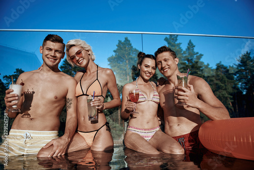 Low angle of young friends drinking beverages while situating in the pool