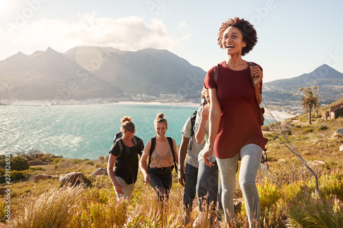Fotografie, Obraz Millennial African American woman leading friends on an uphill hike by the coast