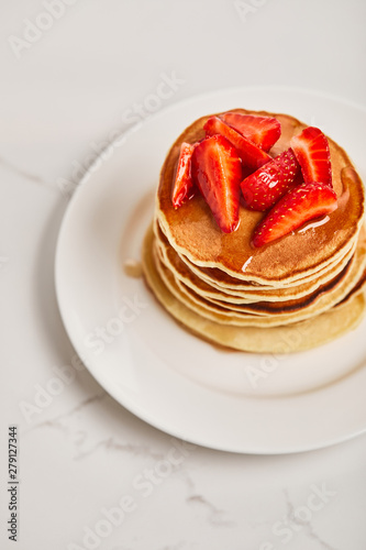 tasty pancakes with strawberries and syrup on white plate on textured surface